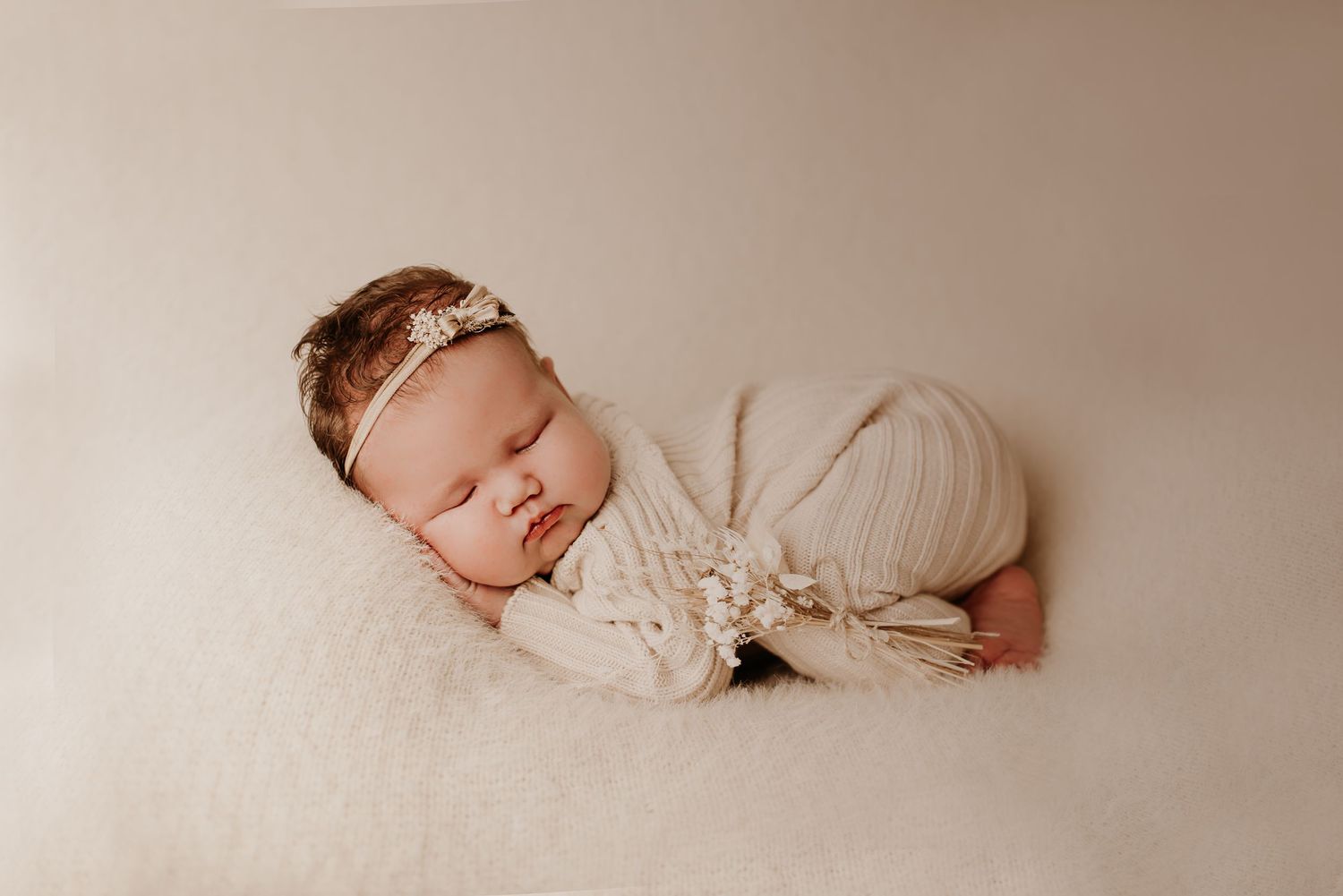 Sleeping newborn in cream wrap and delicate headband during professional photo session.