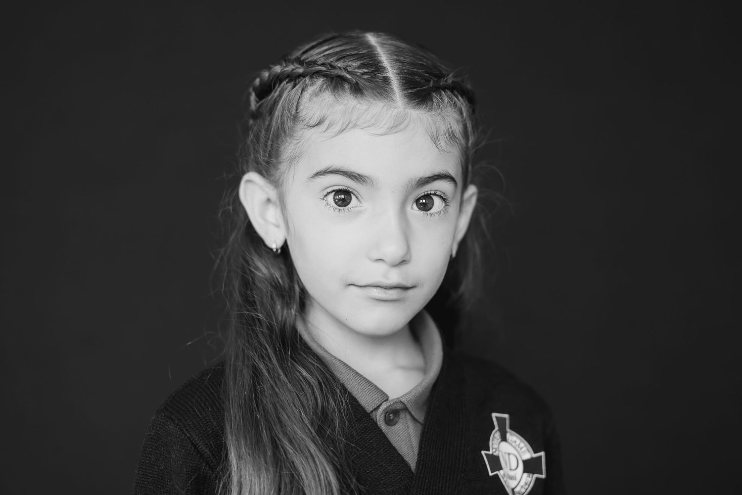 Student wearing dark uniform with long braided hair against black background.