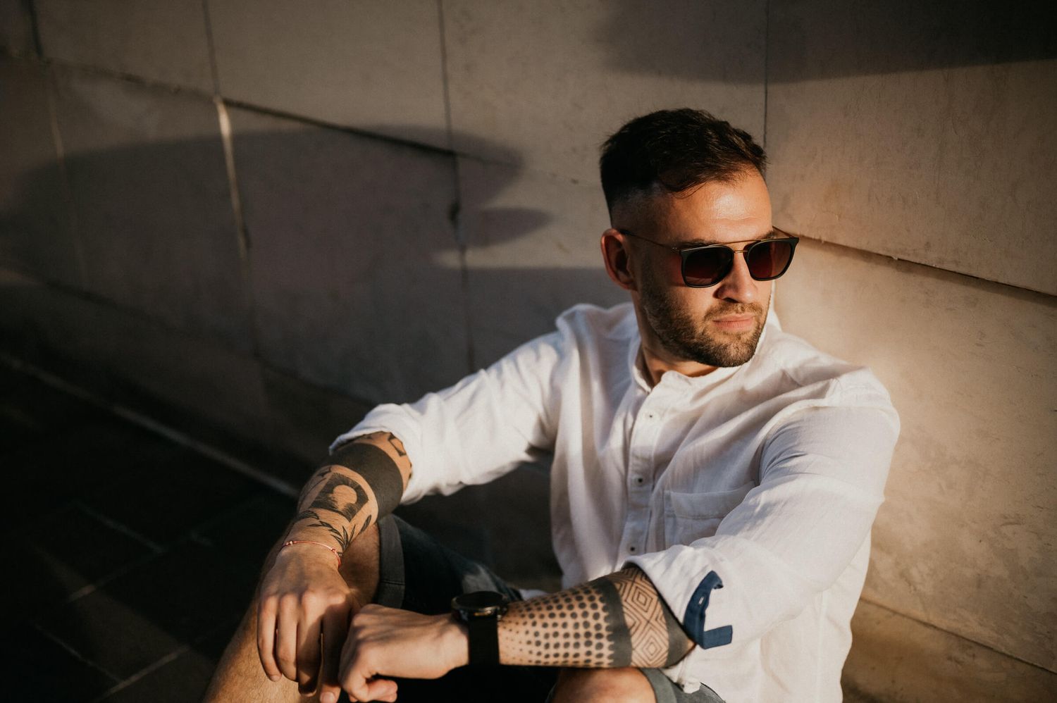 Urban portrait in dramatic lighting showing tattooed arm and sunglasses.