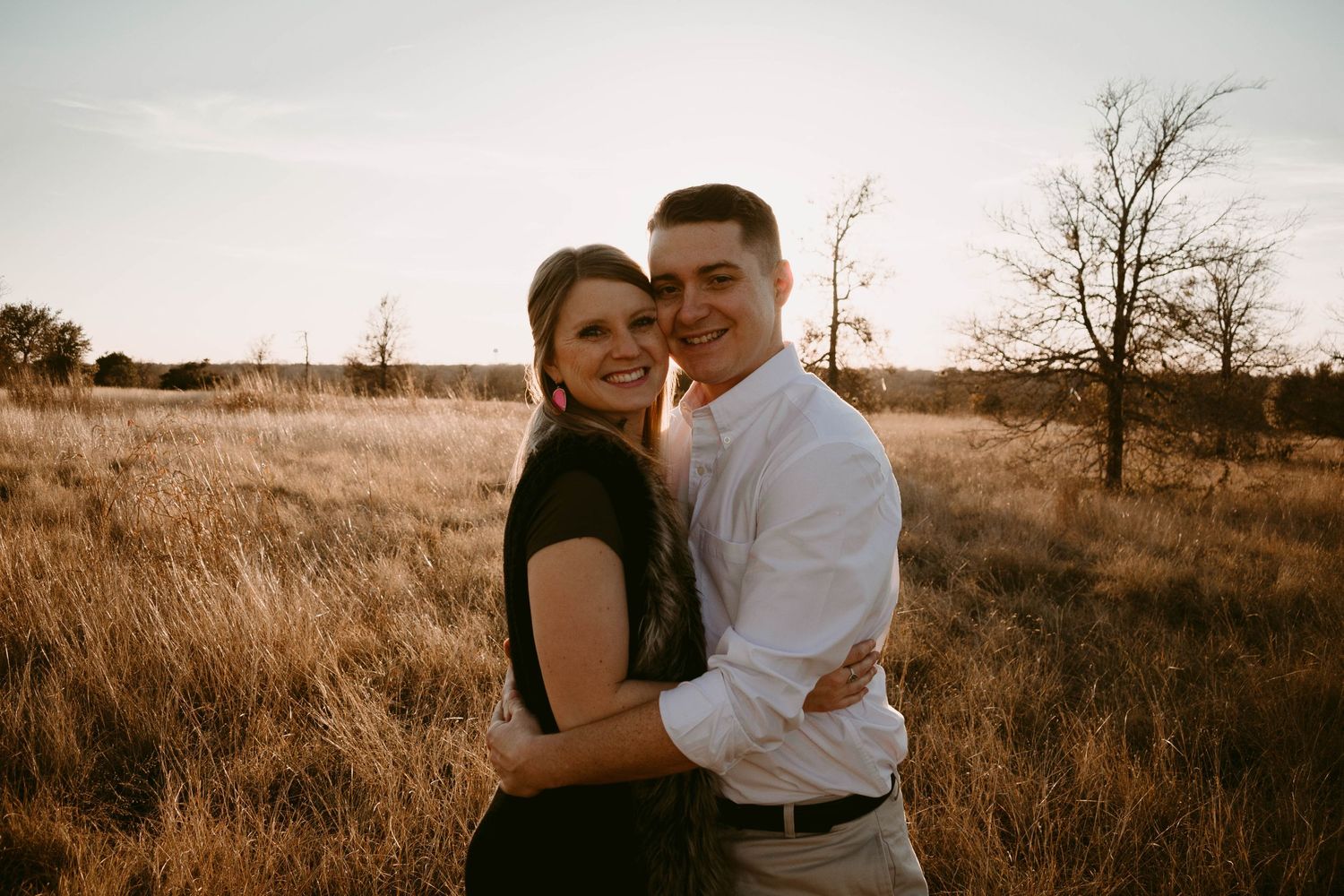 Romantic couple embracing in golden field during sunset photoshoot.