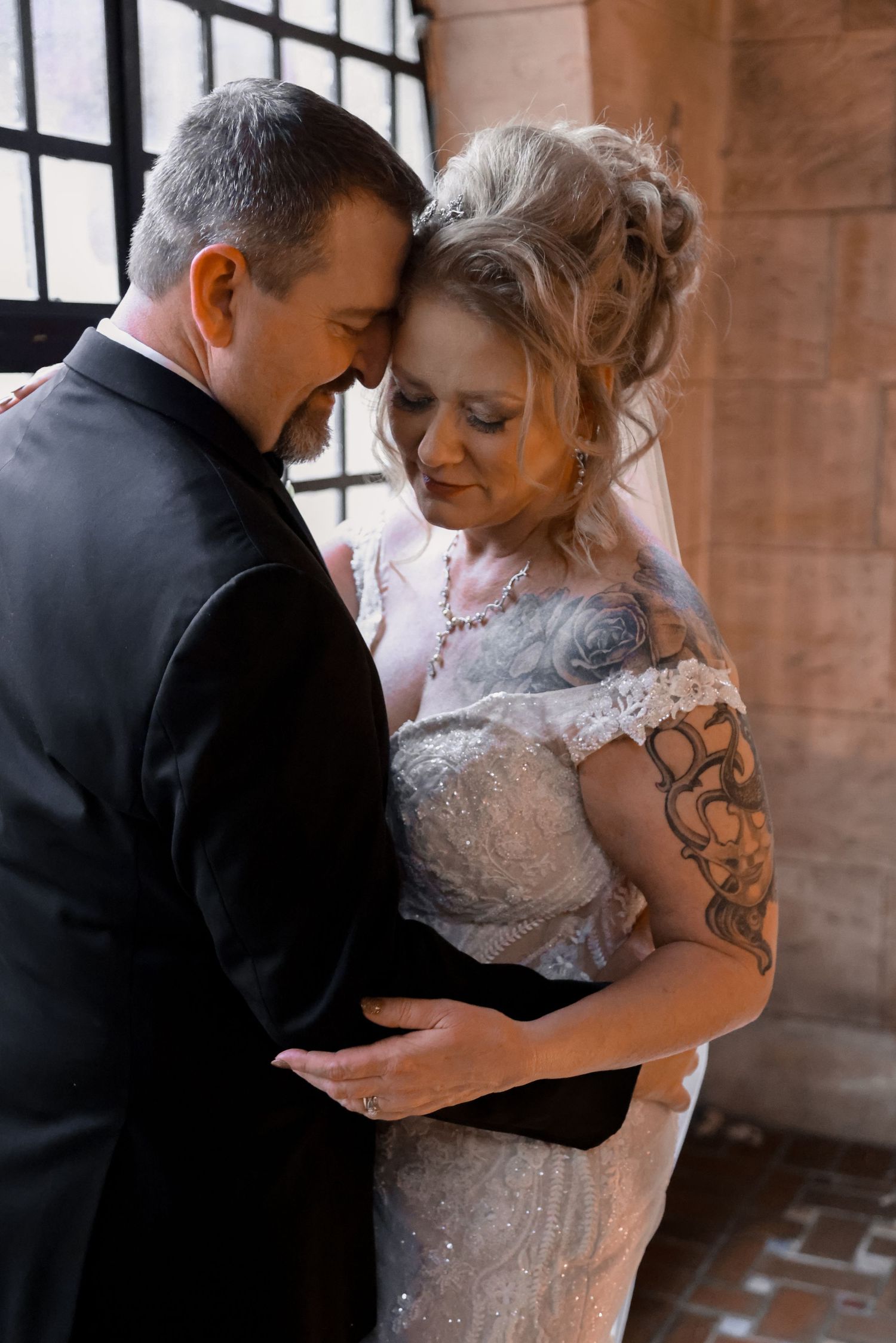 A romantic wedding portrait captures a tender moment between newlyweds in vintage architectural setting.