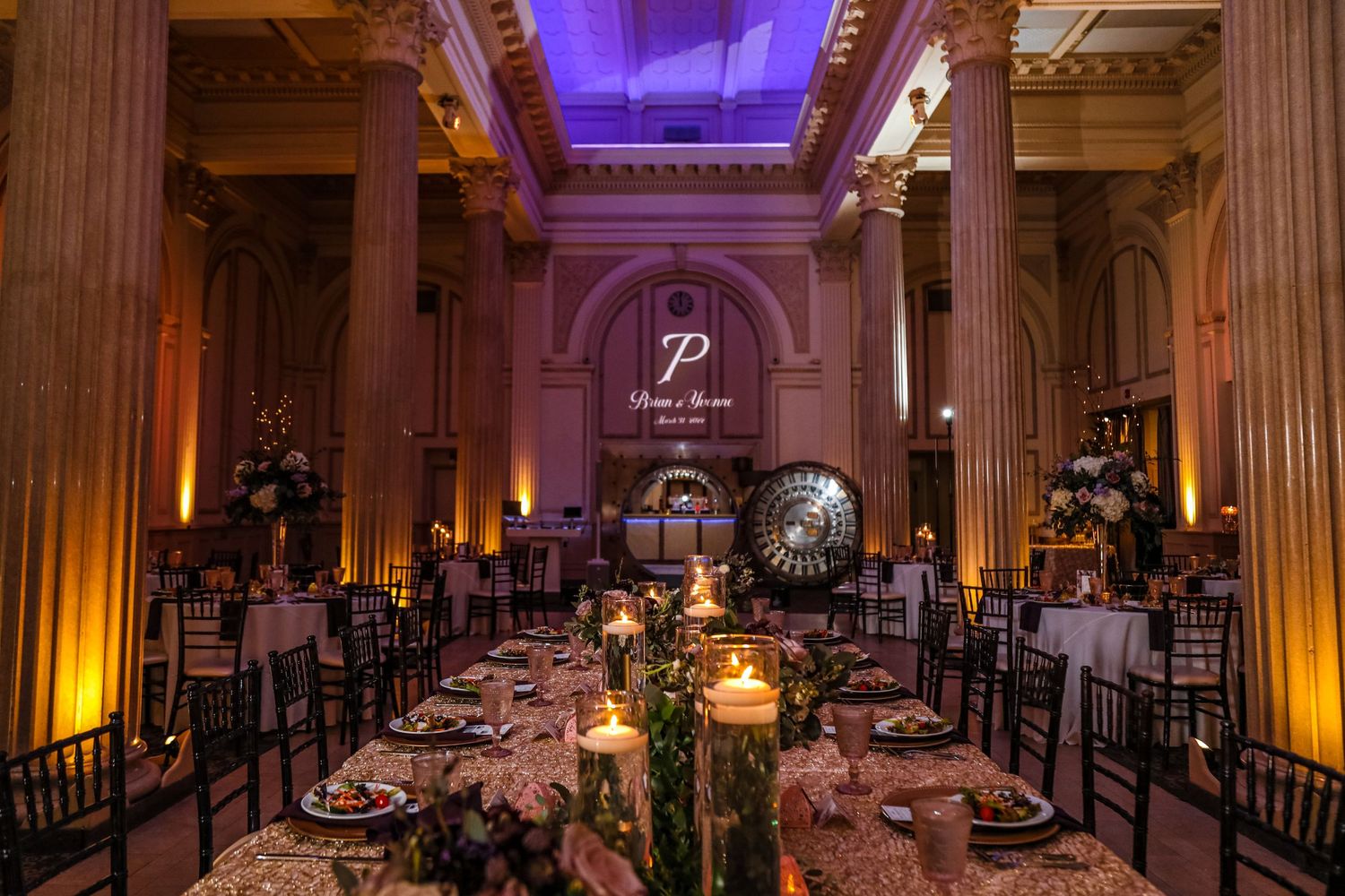 Elegant wedding reception venue with purple uplighting, columns, and candlelit tables set for dinner.