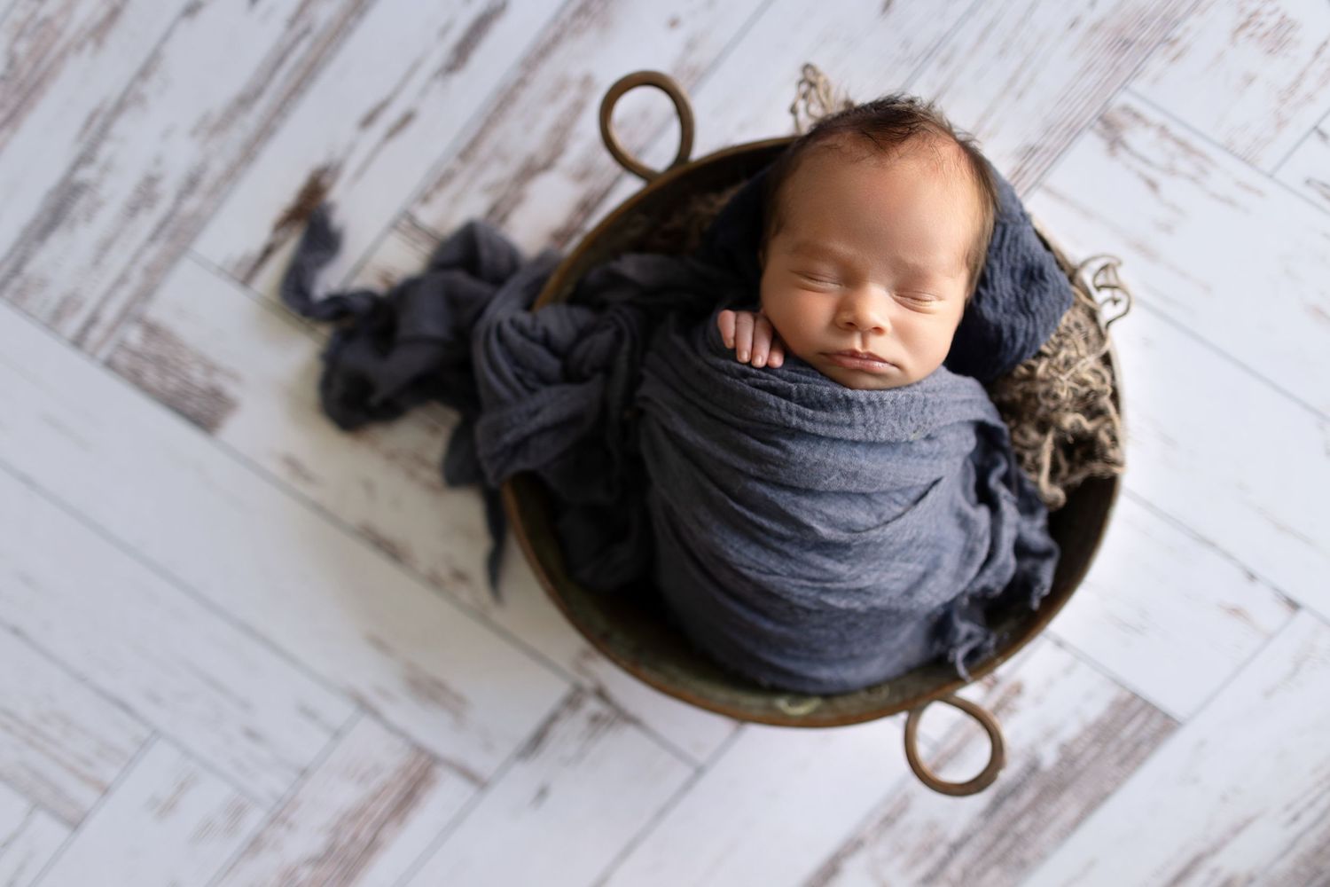 Overhead view of sleeping infant wrapped in grey fabric in vintage metal basket.