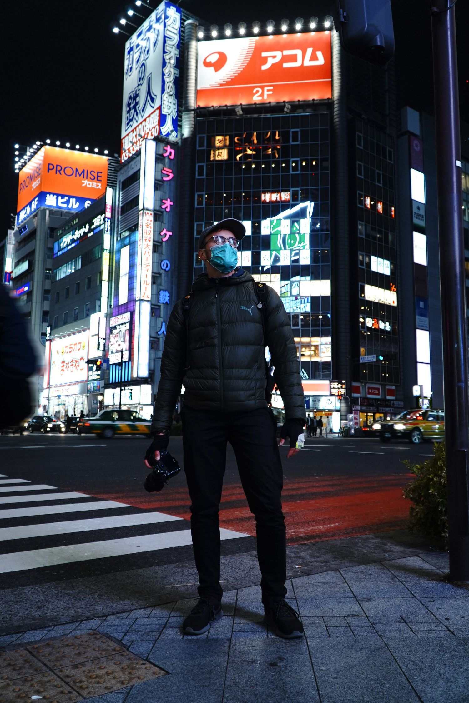 Figure standing on street corner with bright Japanese neon signs and billboards in Tokyo.