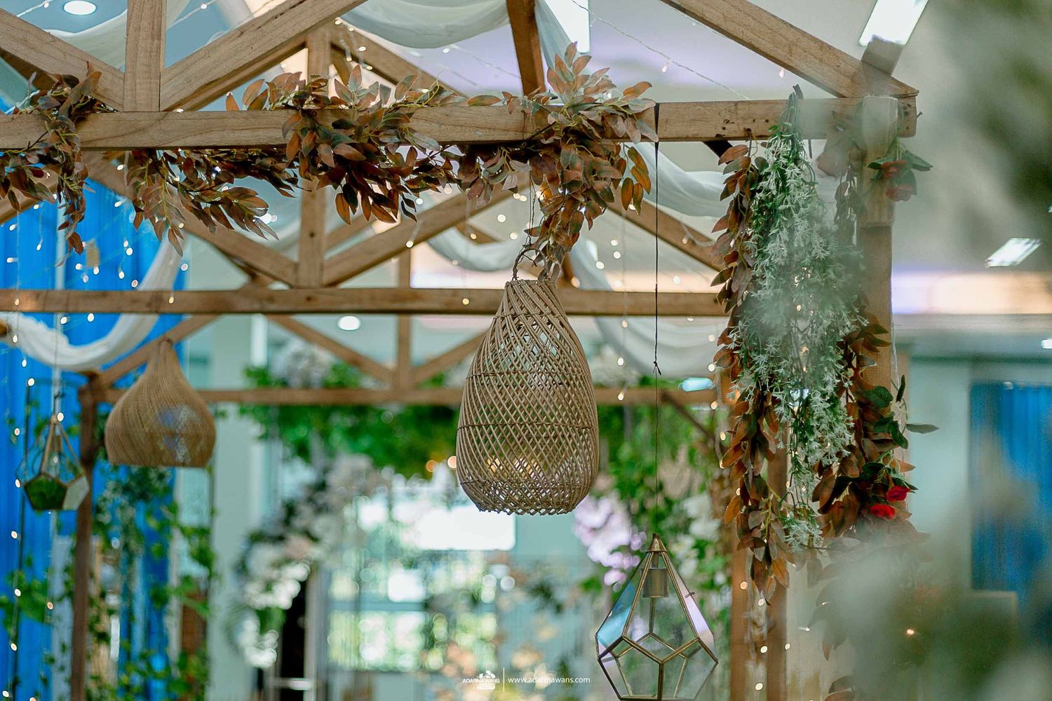 Rustic wedding decor with hanging woven lamp and dried floral arrangements on wooden beams.