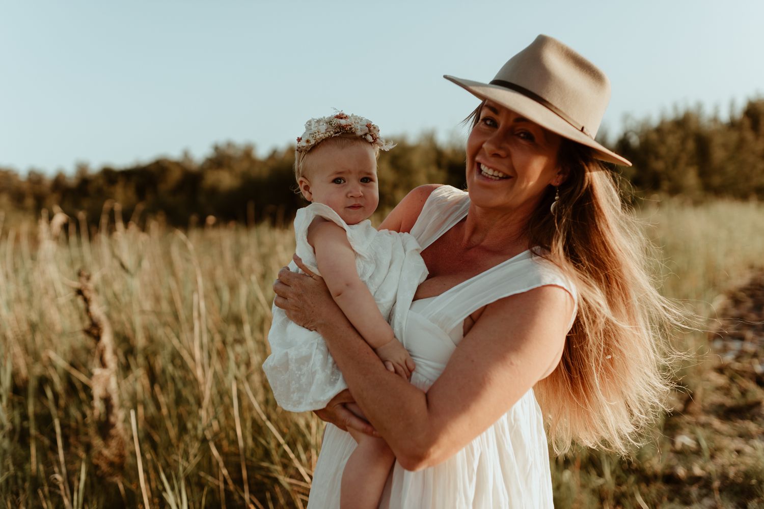 A sweet moment in a sun-drenched field as adults share a laugh while holding a small child.