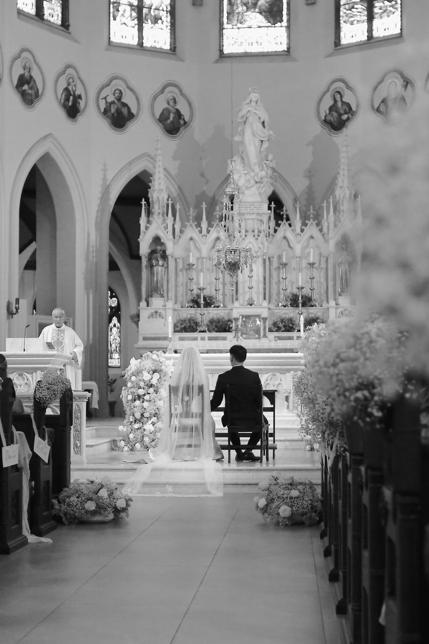 Black and white photo of a church interior during a wedding ceremony with ornate altar decorations.