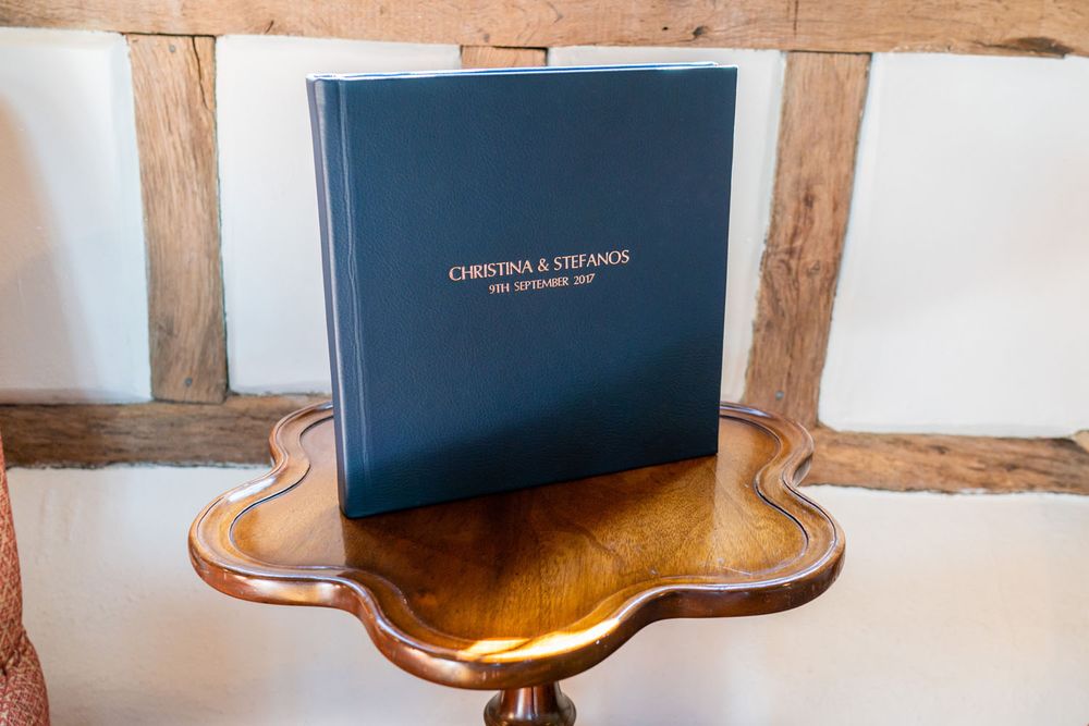 Navy blue leather-bound wedding album sitting on antique wooden table.