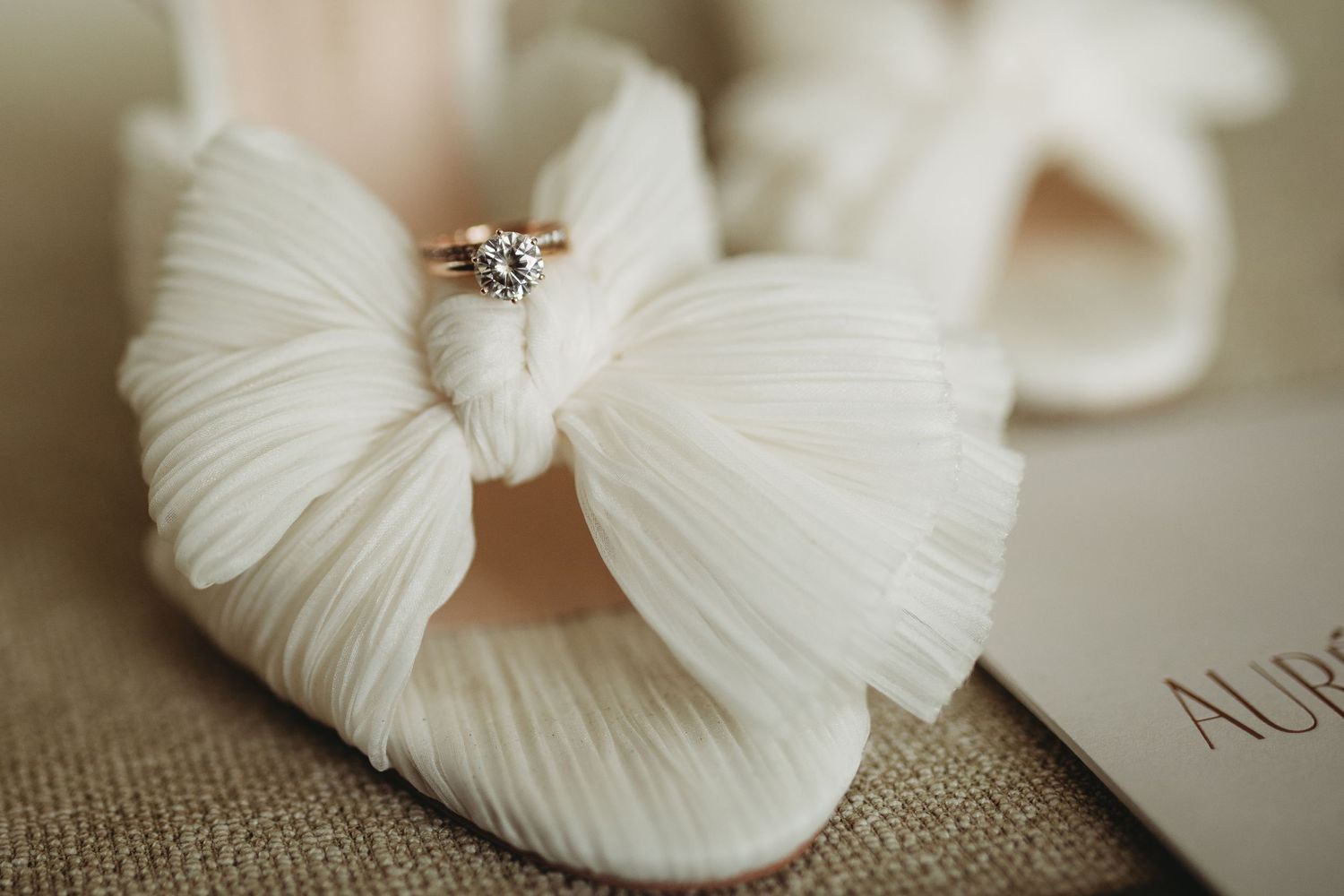 Diamond engagement ring perched on white fabric bow against neutral linen background.