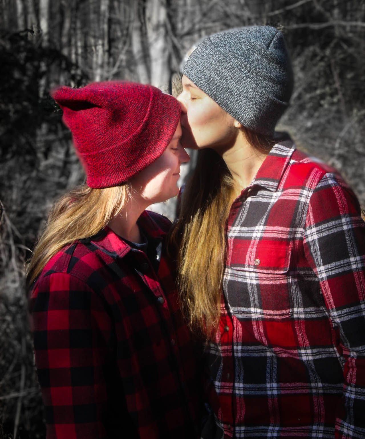 Two people in plaid and winter hats share an intimate moment against a black and white background.