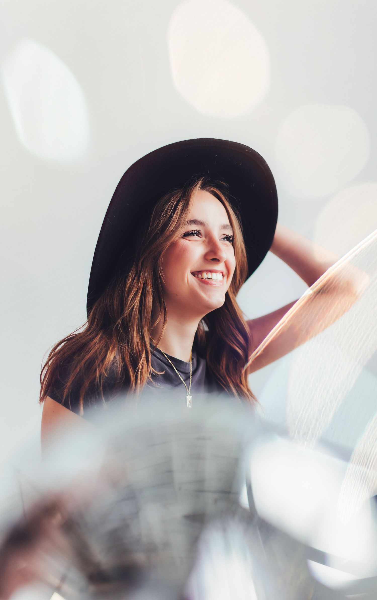 A smiling person wearing a black hat poses against a dreamy bokeh background.