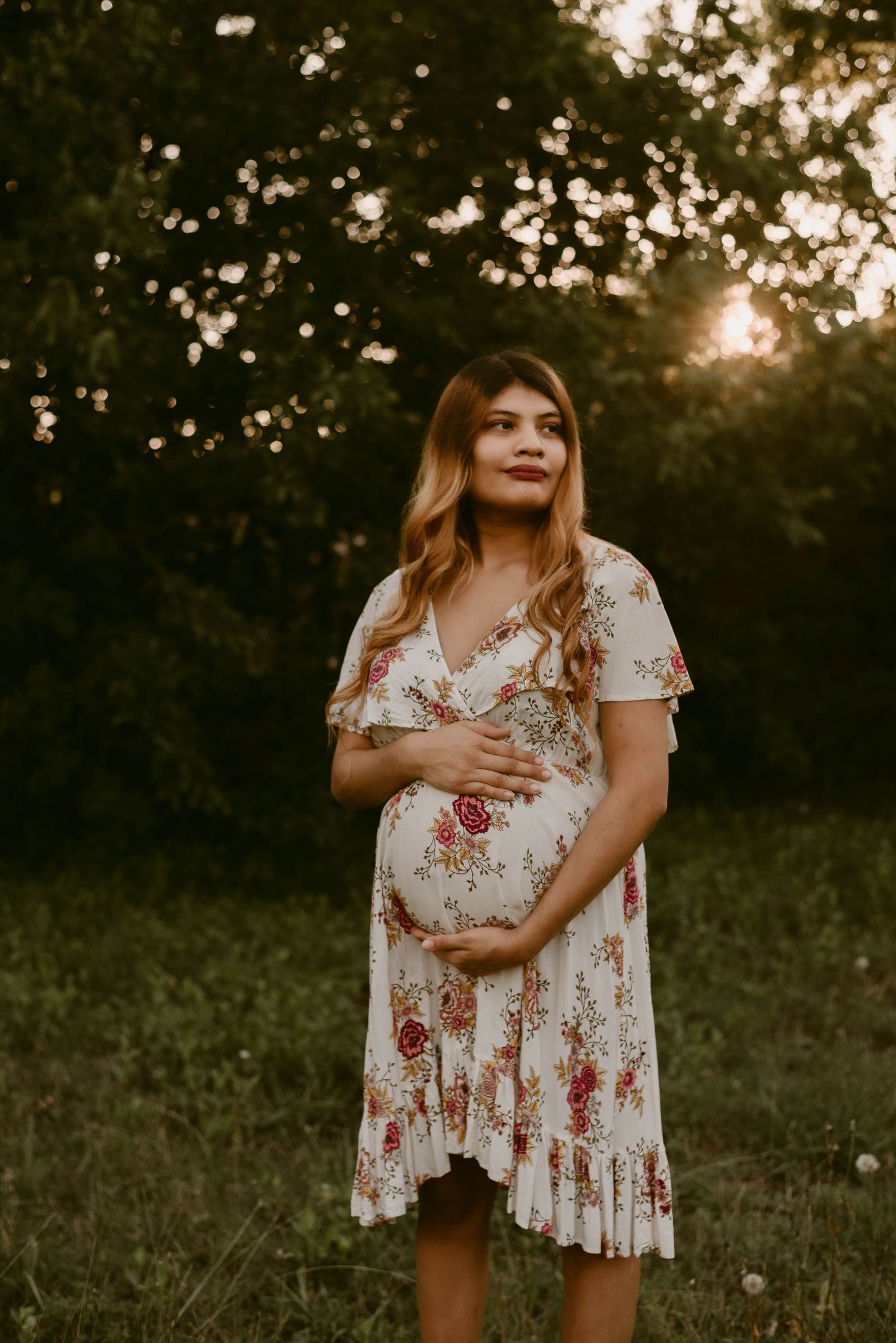 Sunset maternity session featuring white floral dress in natural outdoor setting.