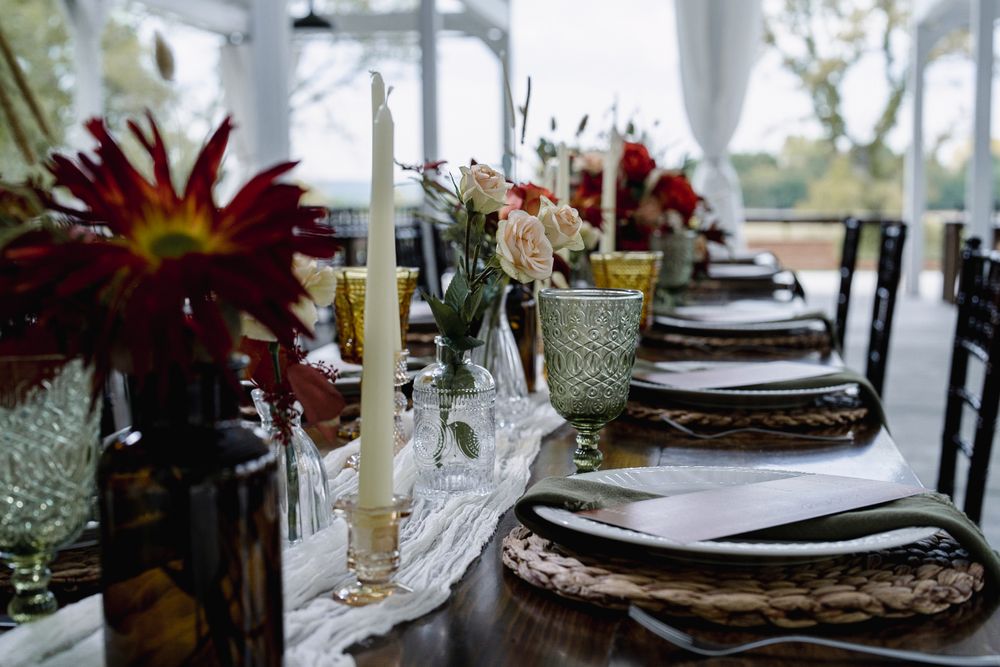 Elegant wedding table setting with red dahlias, taper candles, wicker chargers, and a white lace runner on a dark wood table.