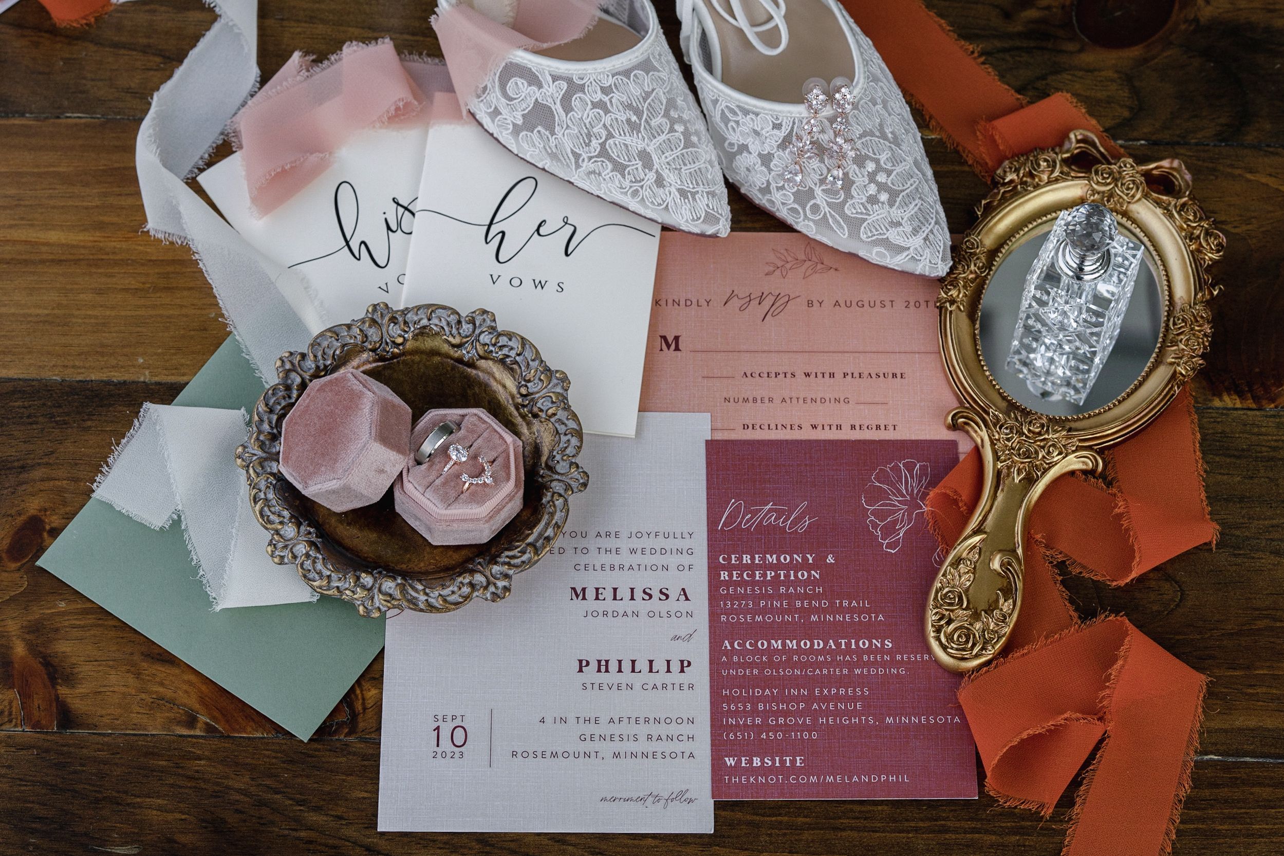 Elegant wedding flat lay featuring lace bridal shoes, pink velvet ring box, floral invitations, and a vintage gold mirror on wood.