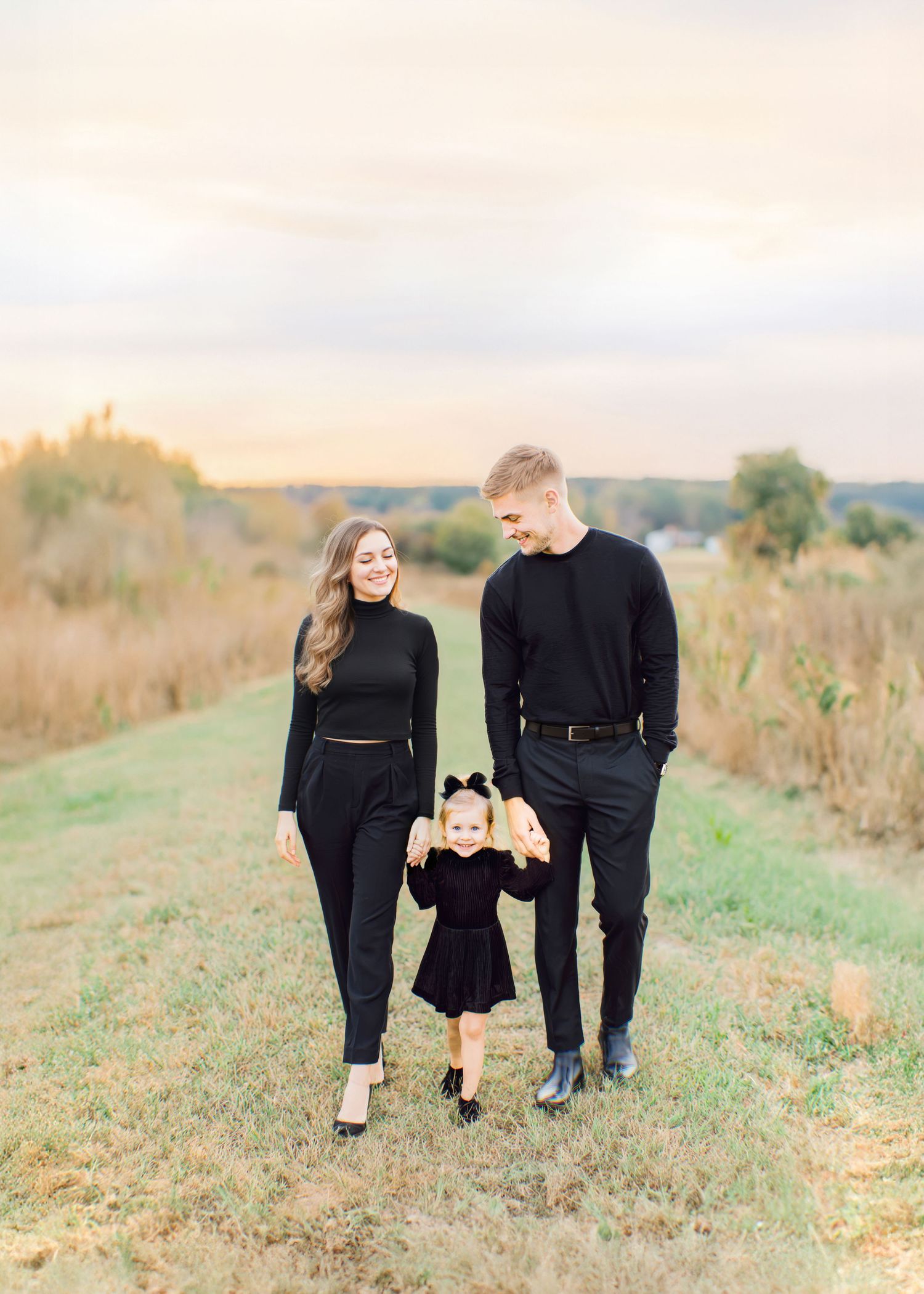 Young family walking together during a fall family photography session in Knoxville, wearing matching black outfits in an open field.