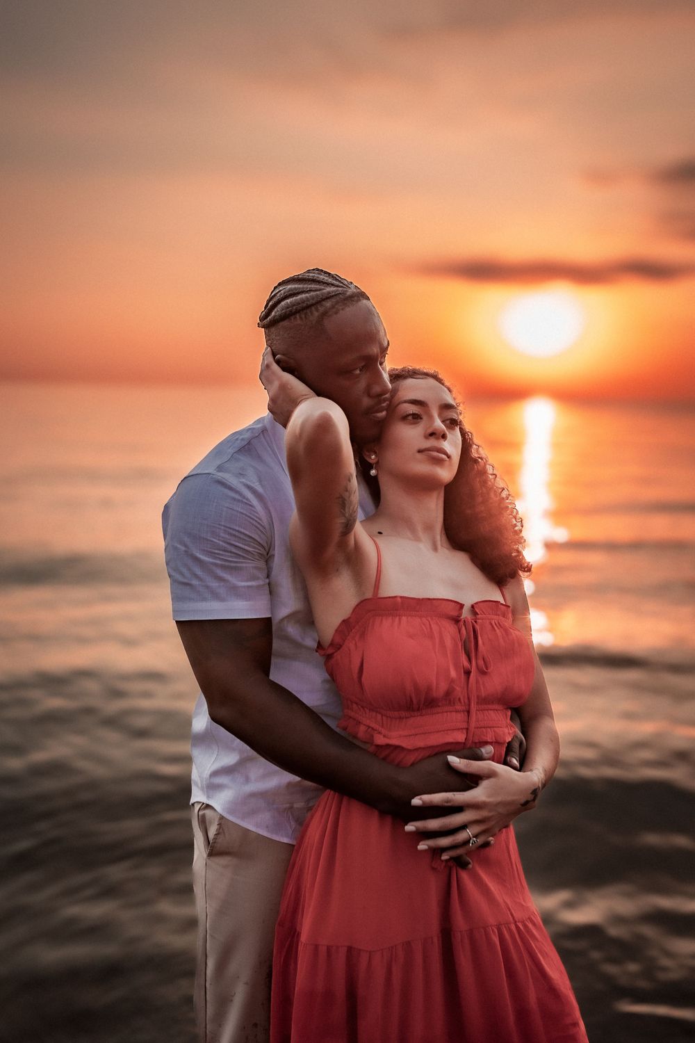 Couple in romantic embrace during sunset at beach with orange sky.