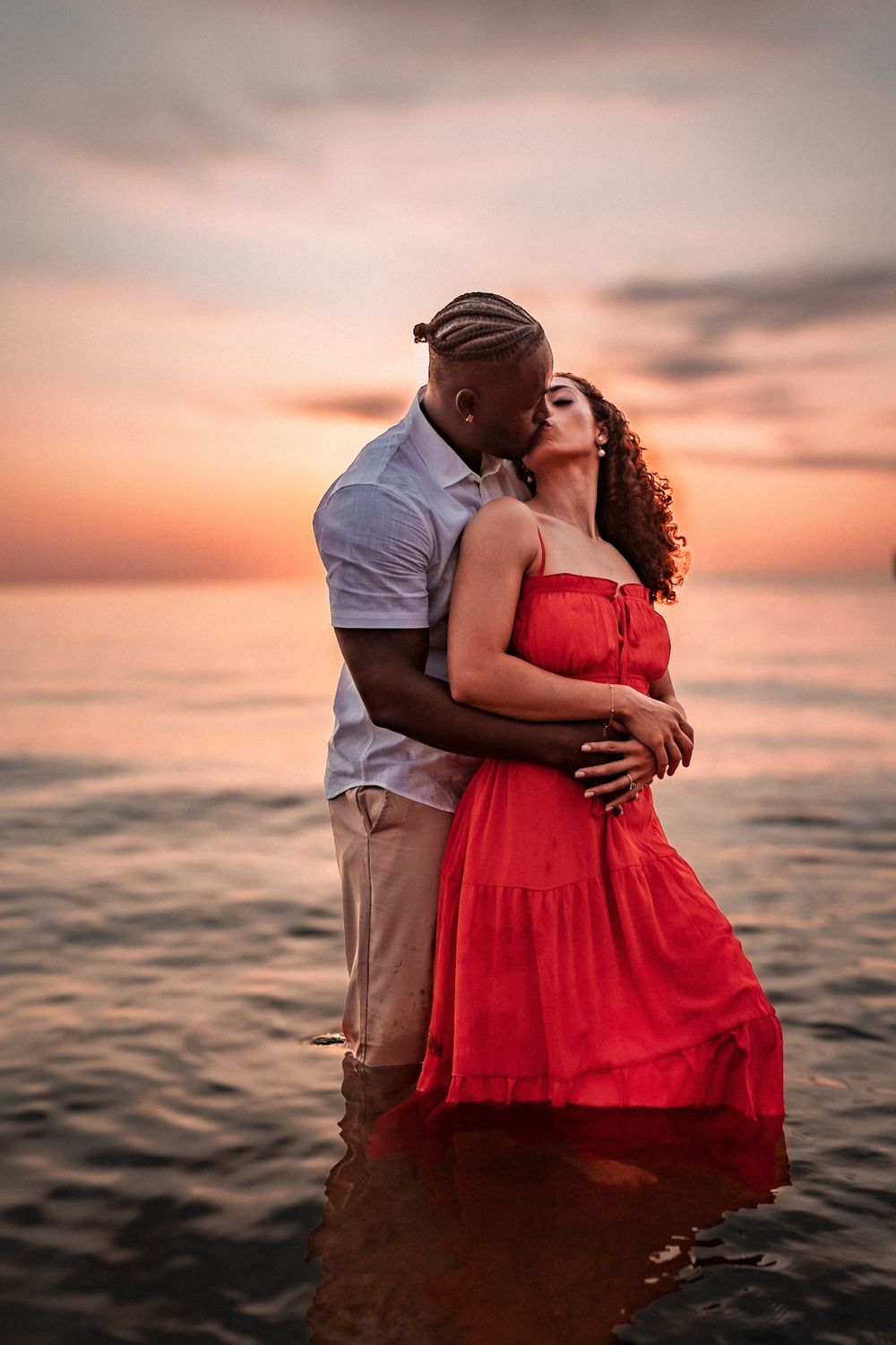 Couple in water during sunset, wearing red dress and white shirt.