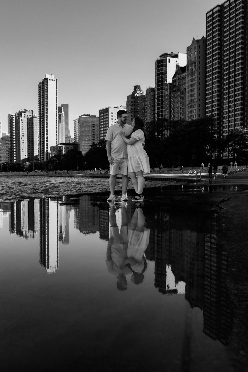 Black and white photo of couple embracing with city skyline reflection in water.