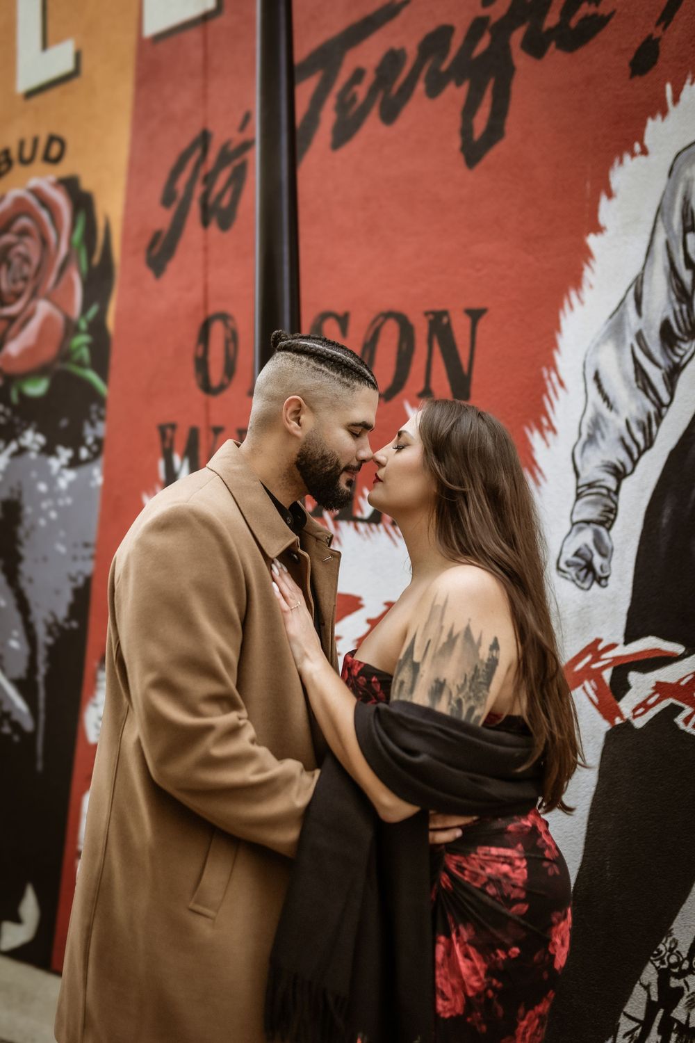 A romantic couple embraces against a vibrant wall mural featuring roses and graffiti art.