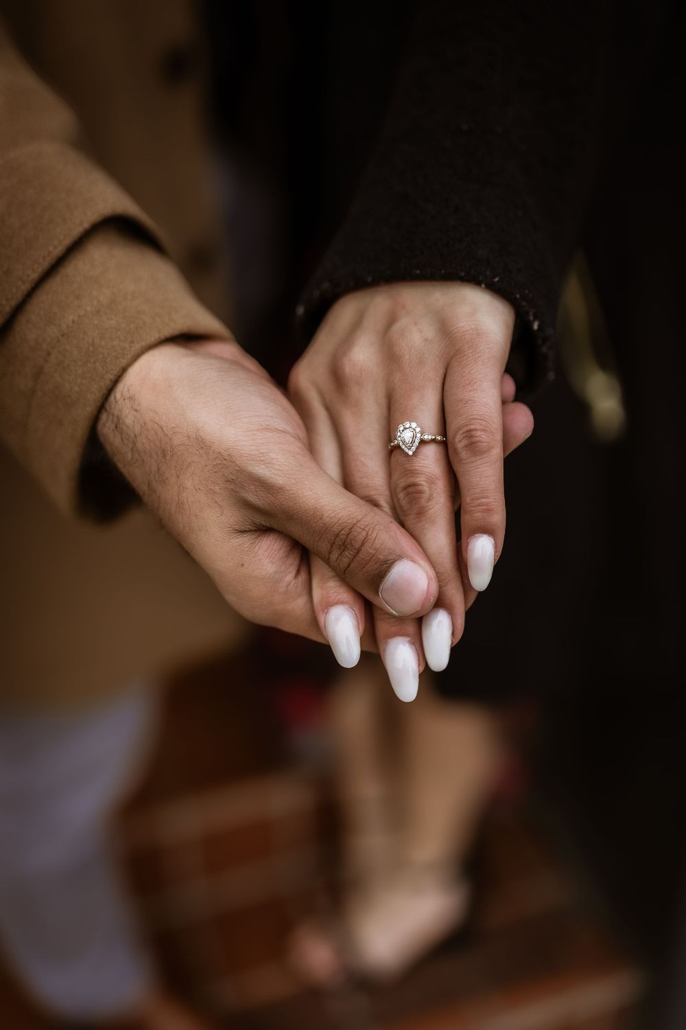 Close-up of hands holding with an engagement ring and white manicured nails.