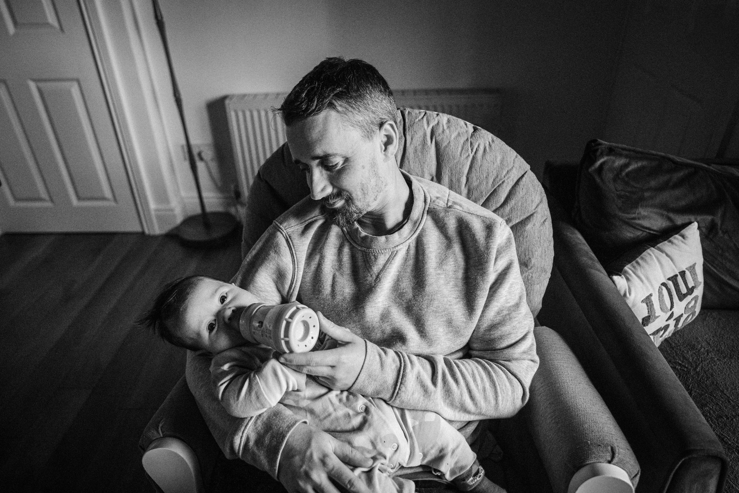 A tender black and white moment captured between parent and infant in a cozy armchair.