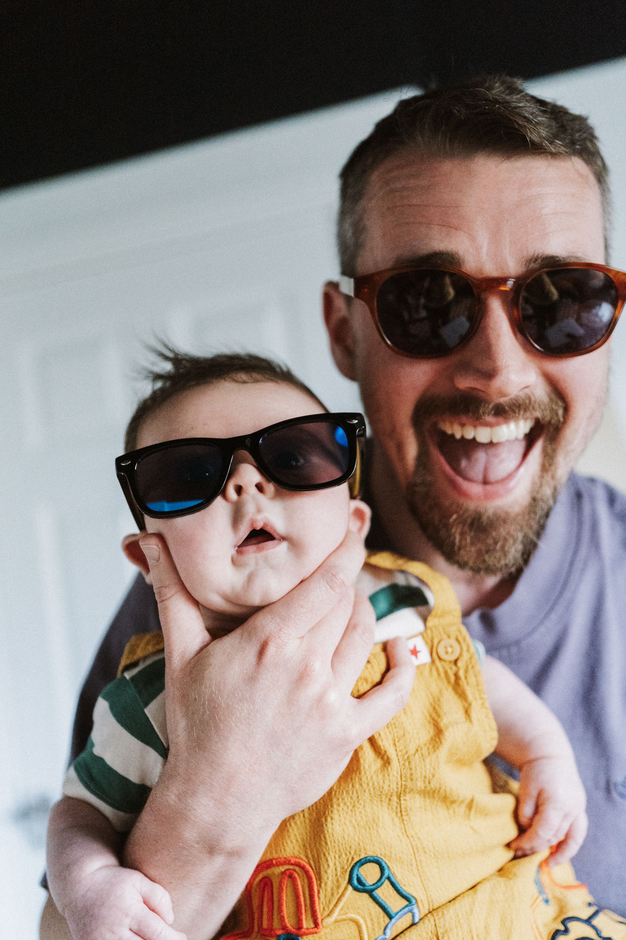 Two people wearing sunglasses share a joyful moment while wearing casual attire.