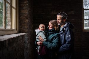 A family shares a tender moment together by a window in a rustic brick interior space.