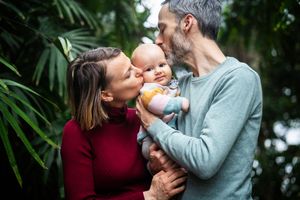 A couple shares tender moments together in a garden setting with lush greenery in the background.