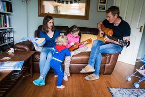 People sitting on hardwood floor in a living room with natural light coming through window.