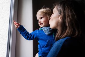 Parent and child looking out window together in blue sweater creating tender moment.