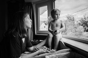 A series of black and white photographs showing intimate moments between a parent and child by a window.