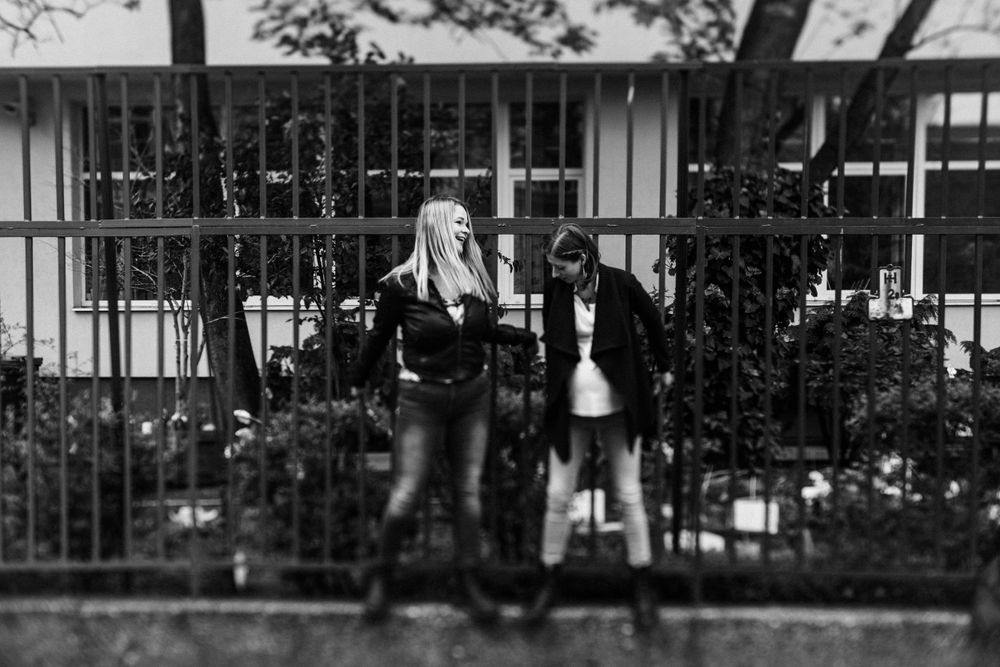 A black and white photo of two people posing against decorative metal fencing.