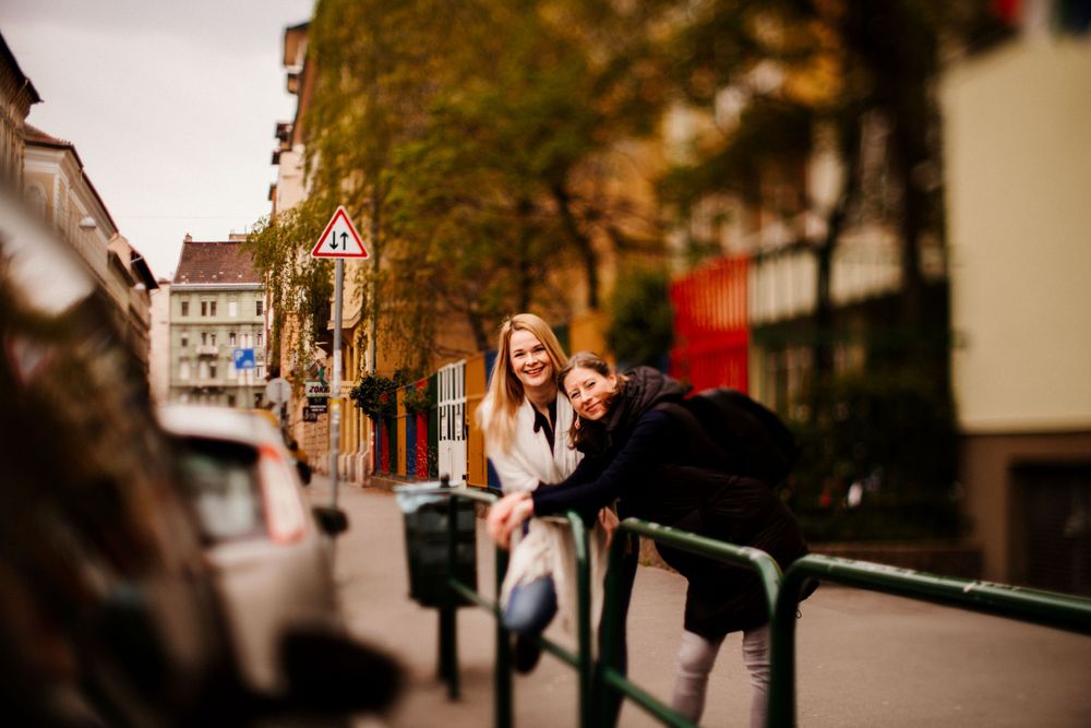 Two people playfully posing on metal railings along an autumn street.