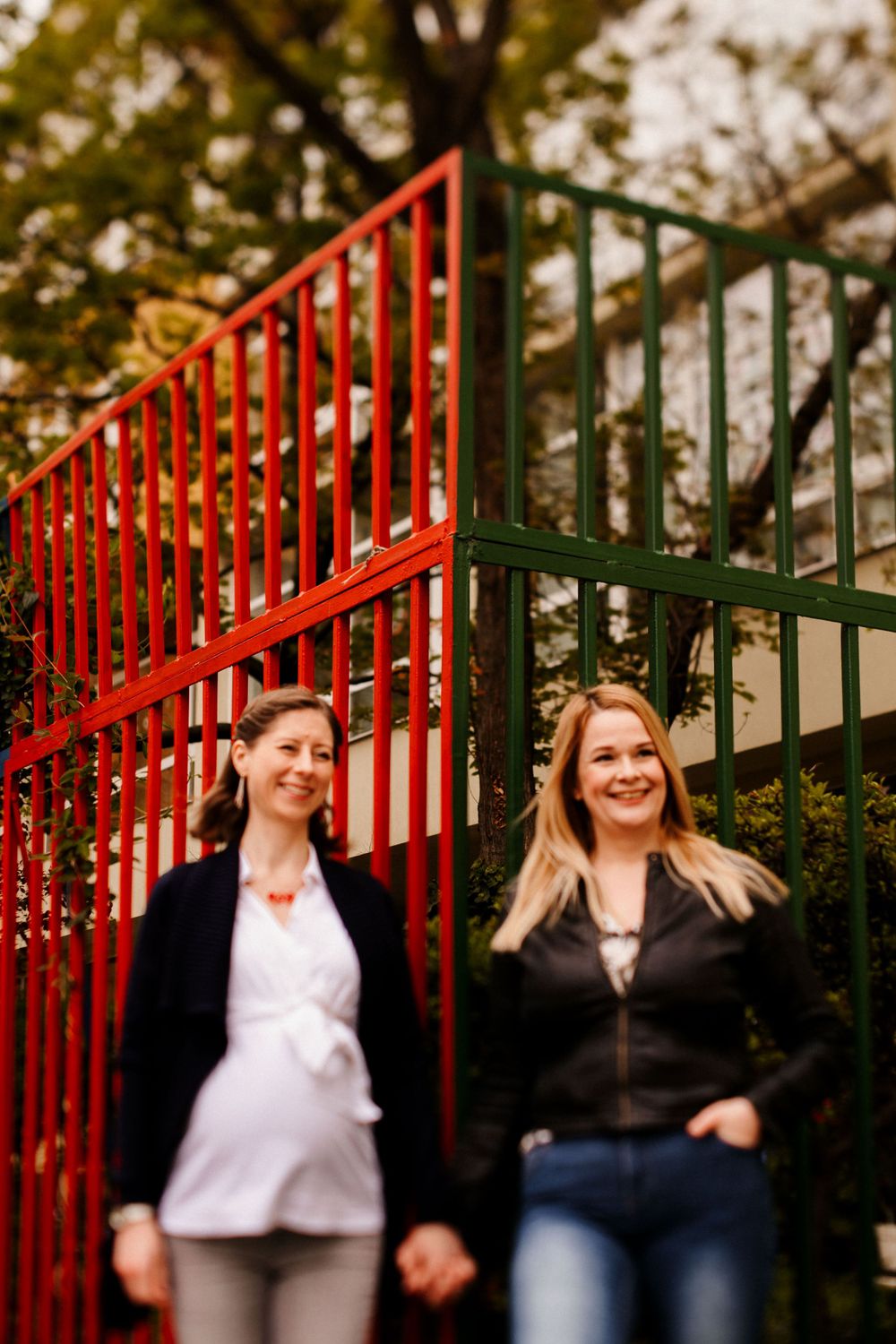 Two people stand by red and green metal railings during autumn, sharing a cheerful moment.