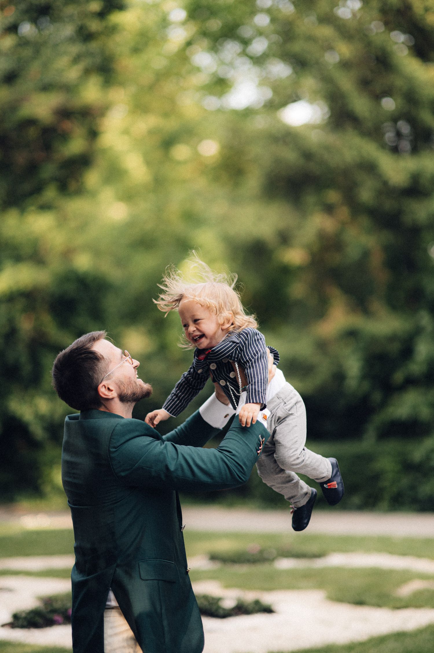 A playful moment captured outdoors as an adult lifts a child in the air against trees.