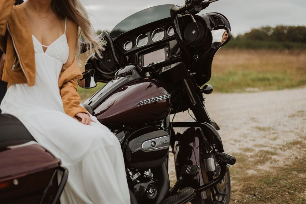 Close up view of a maroon Harley Davidson motorcycle with riders in casual attire.