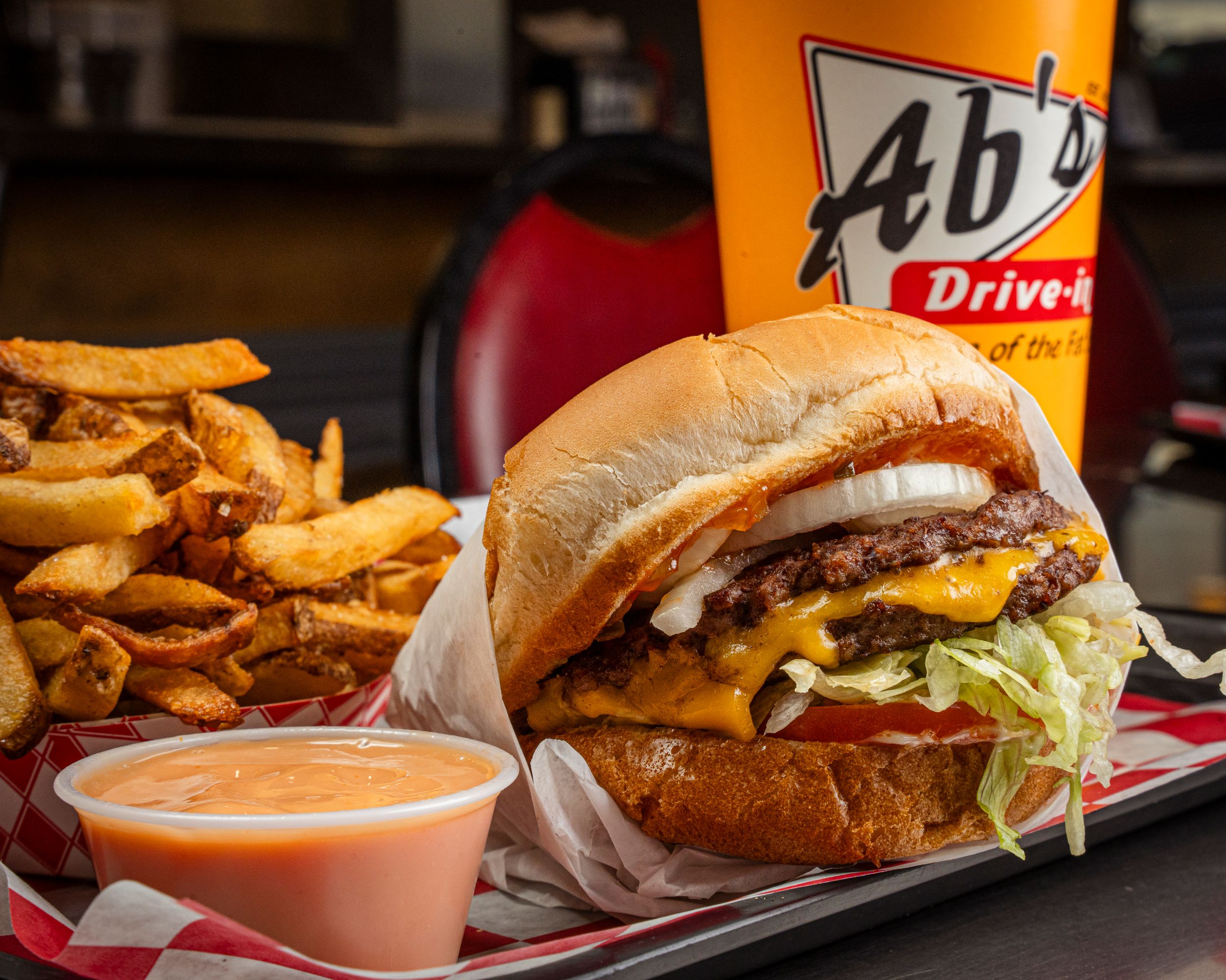 Double cheeseburger with fries and dipping sauce served at Ab's Drive-In restaurant on checkered tray.