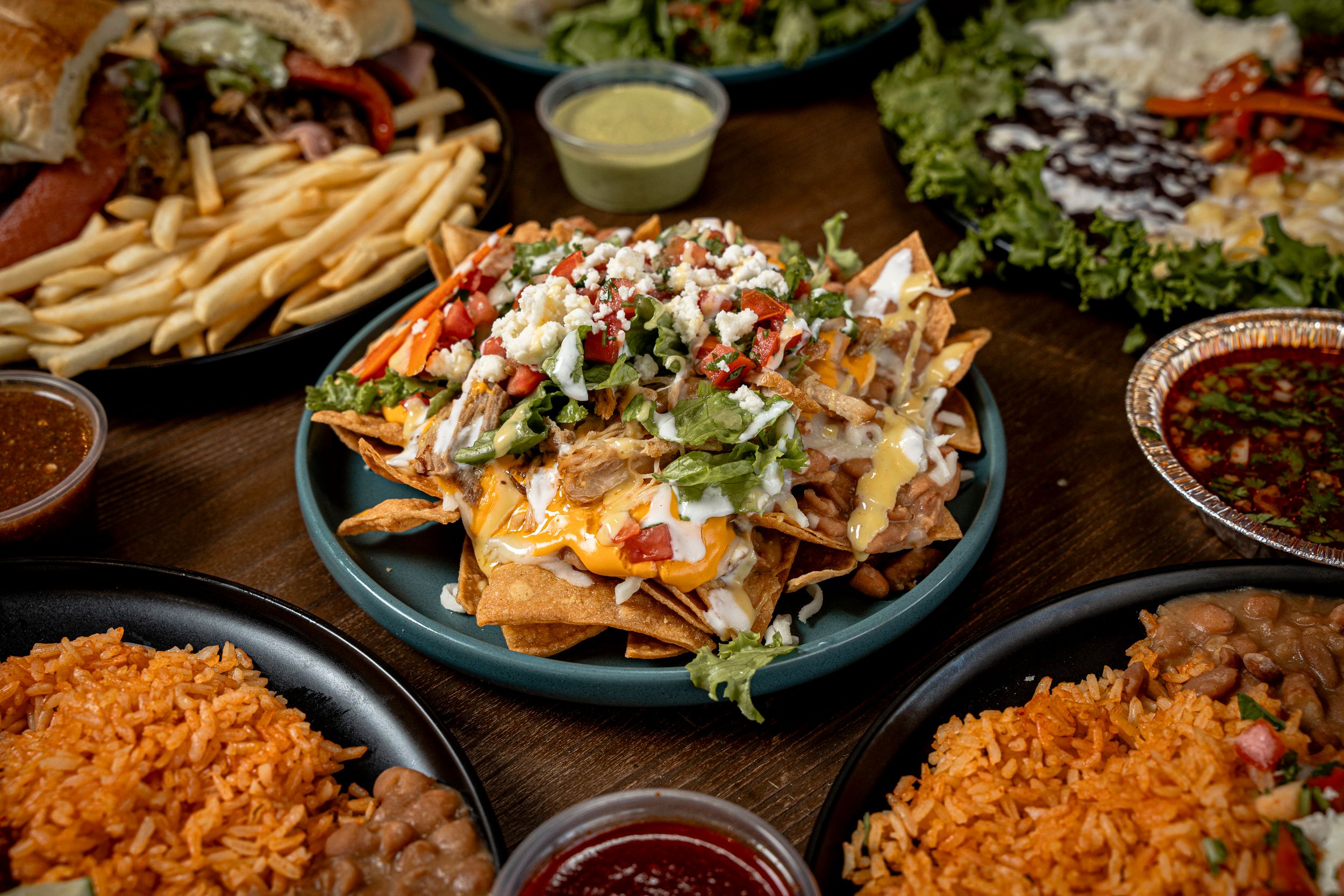 Loaded nachos topped with cheese, lettuce, and toppings surrounded by Mexican sides and salsas.