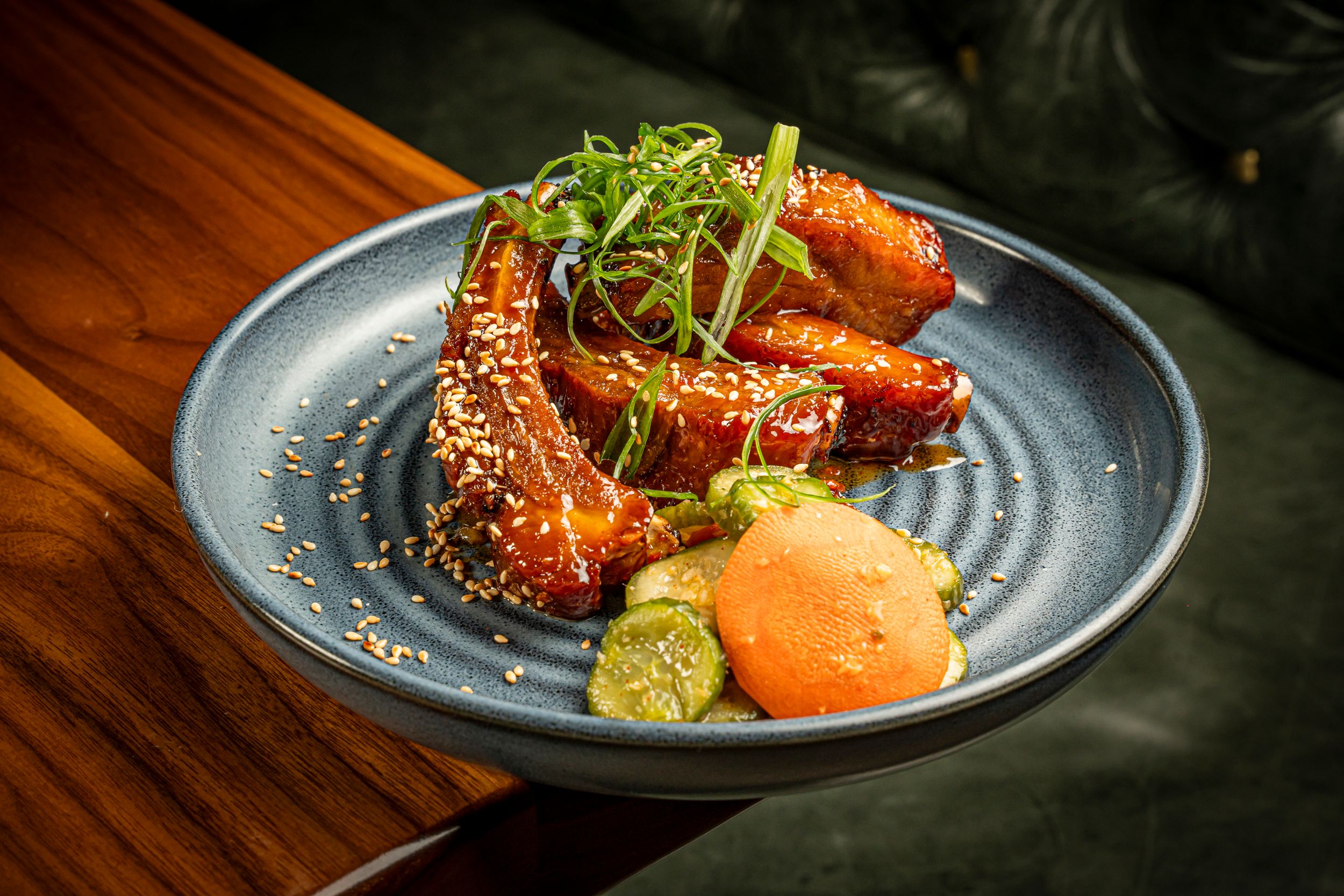 Glazed chicken wings topped with sesame seeds and microgreens served with citrus garnish in blue bowl.