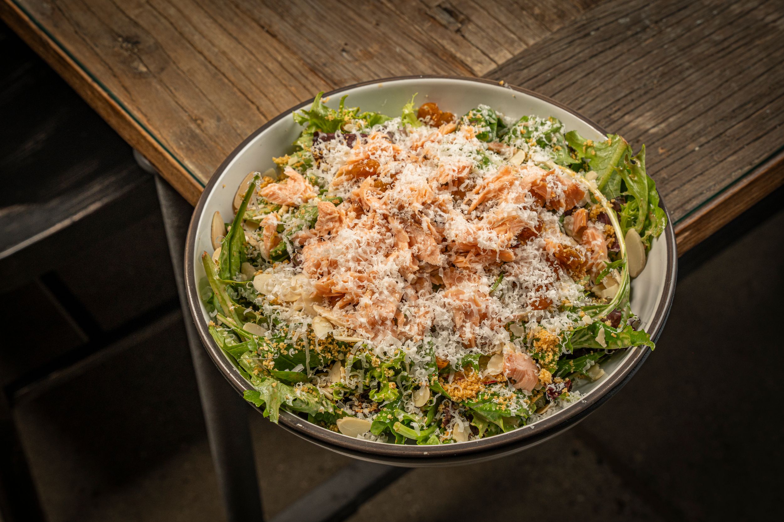 Fresh Caesar salad topped with grilled chicken, shaved parmesan, and croutons in a rustic wooden bowl.