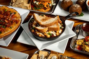 Cast iron skillet with toasted bread and mixed ingredients surrounded by assorted appetizer dishes.