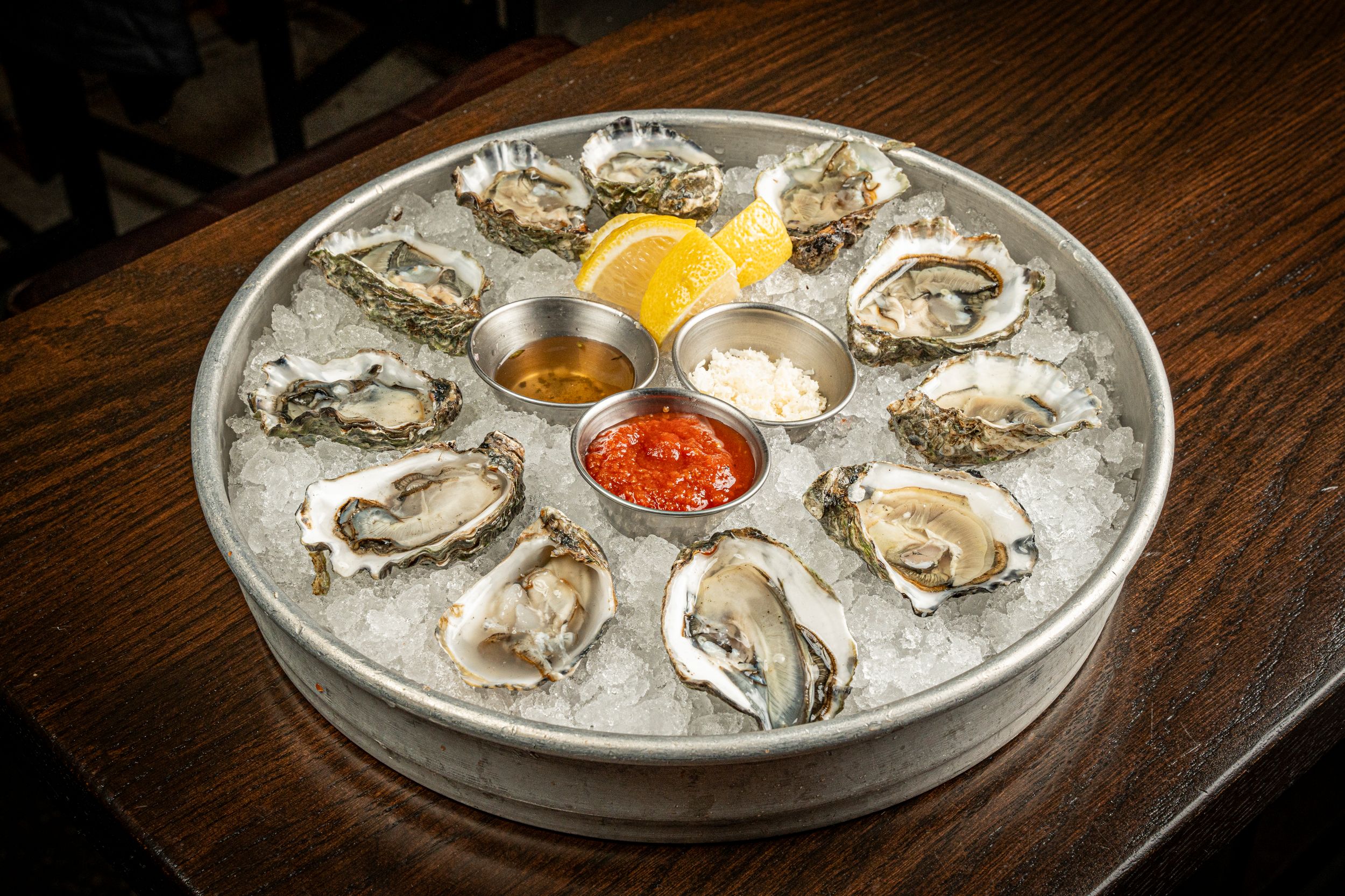Fresh oysters on the half shell served on ice with lemon wedges and cocktail sauce on a round platter.