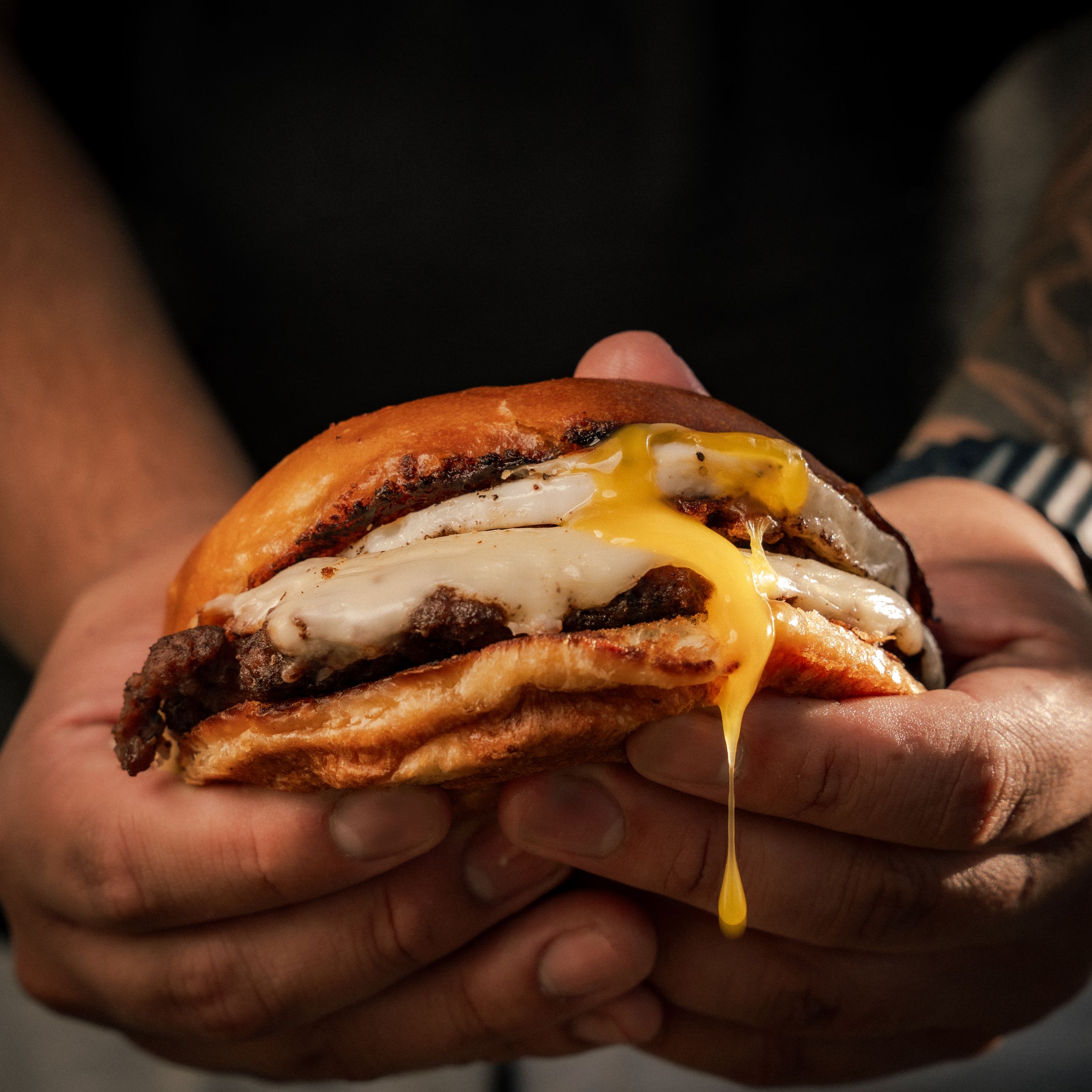 Hands holding a juicy cheeseburger with melted cheese dripping from a toasted brioche bun.