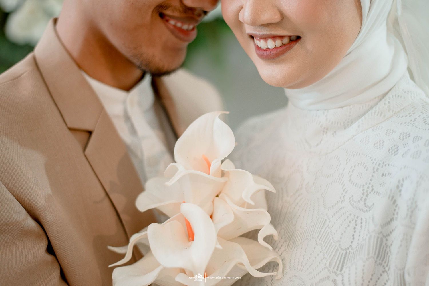 Close up of delicate white calla lily bouquet held between couple in beige and white attire.