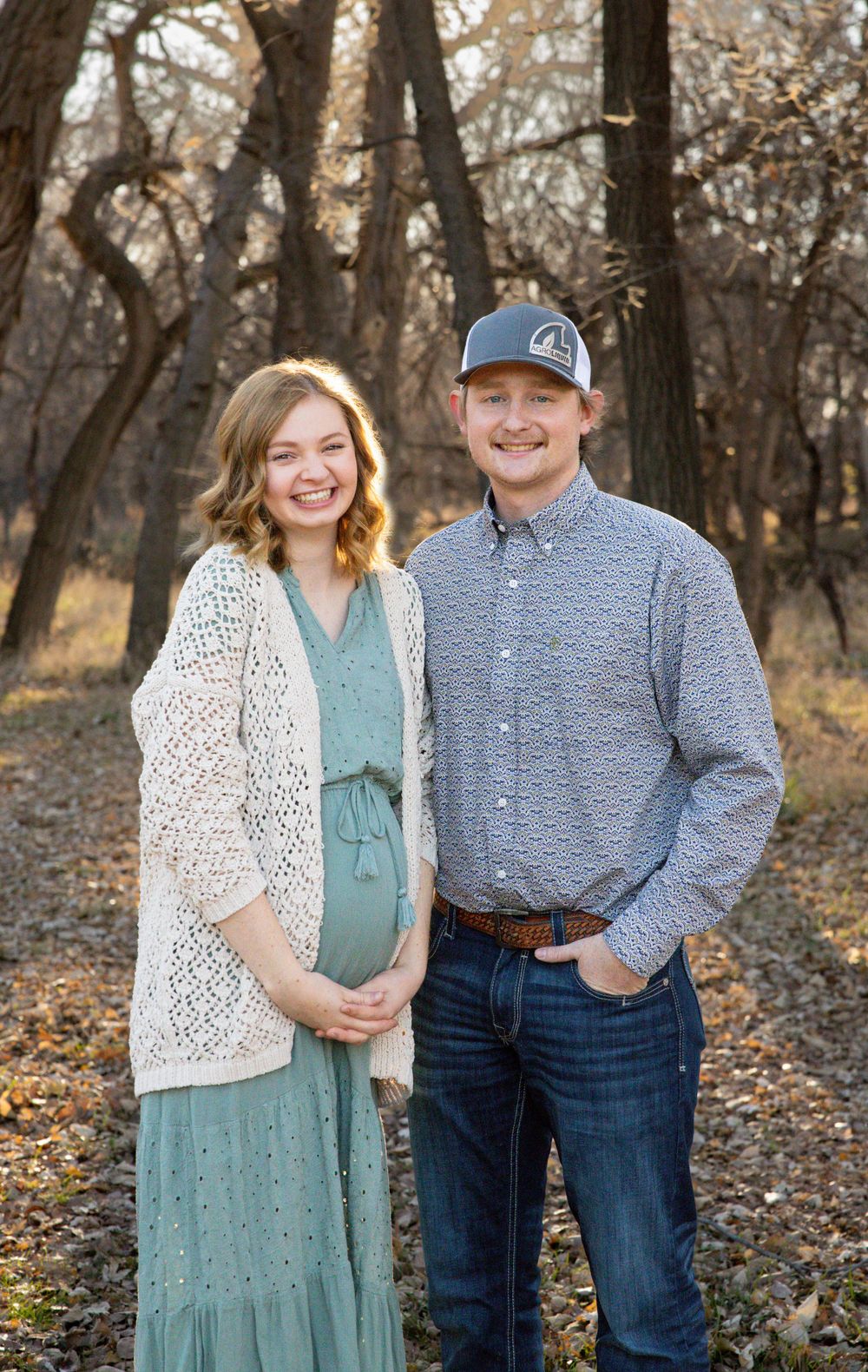 A couple poses for autumn photos among fallen leaves in a wooded setting.