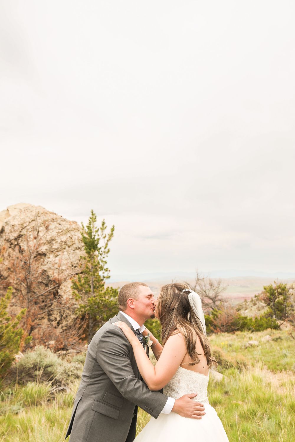 A couple in wedding attire share an intimate moment against a scenic mountain backdrop.