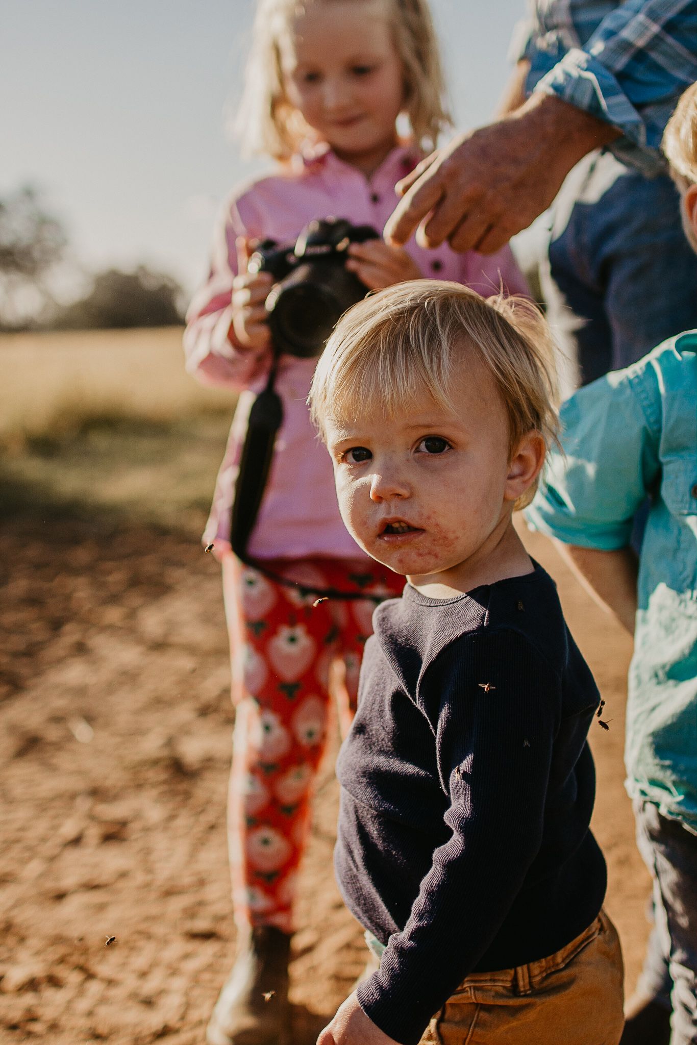 young farm boy with a grubby face holding dads hands in the paddock.