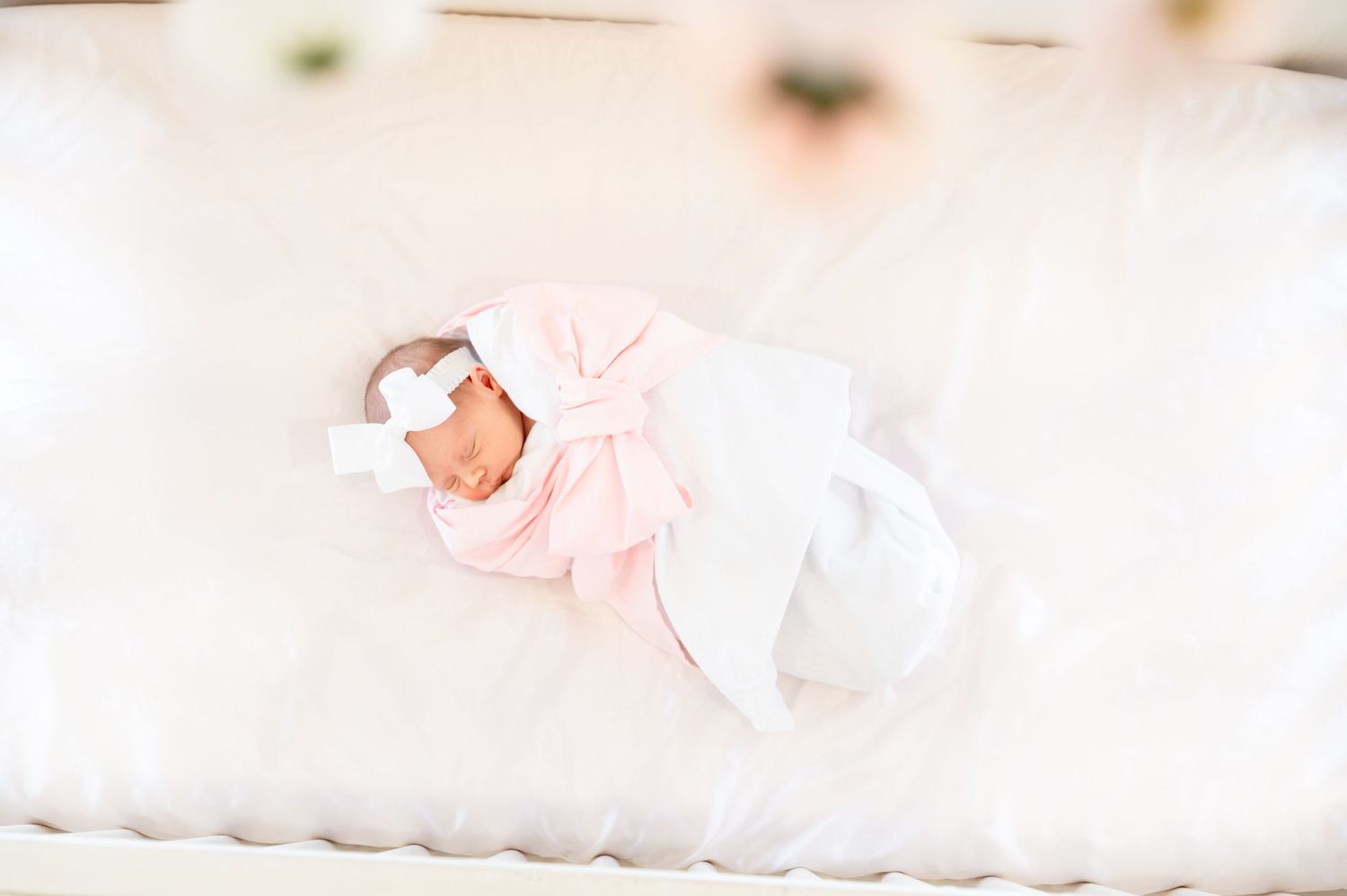 arial shot of a newborn baby girl sleeping in a white wrap and pink bow in a light and bright lifestyle newborn session