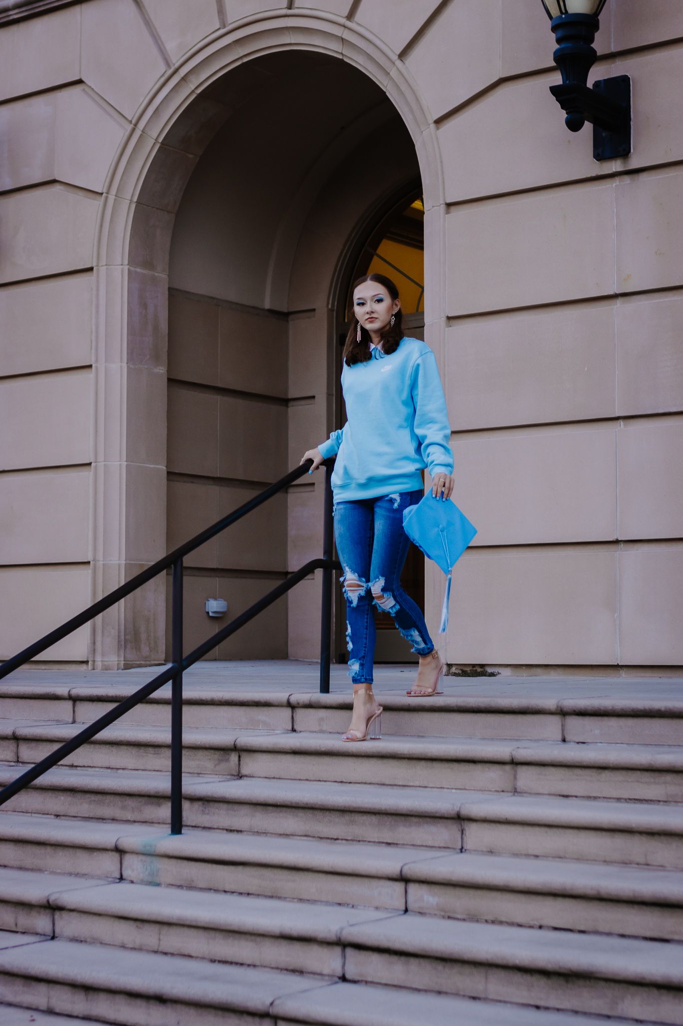 Person wearing bright blue sweater and jeans descends stone steps in front of classic architecture.
