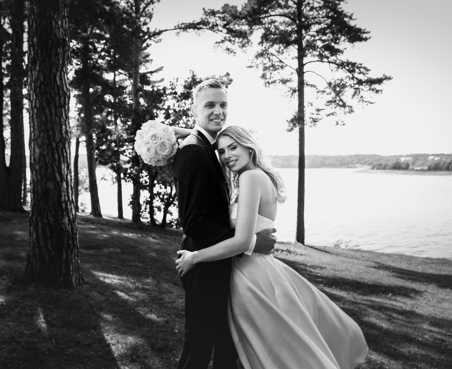 Black and white wedding portrait with pine trees and lake vista in the background.
